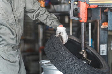 タイヤチェンジャーを使いタイヤの組み替えをするメカニック・整備士の男性作業員
