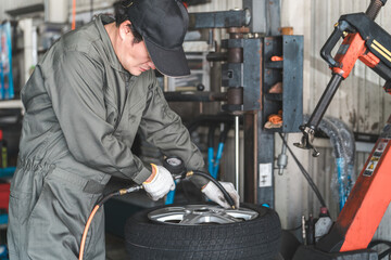 タイヤチェンジャーを使いタイヤの組み替えをするメカニック・整備士の男性作業員
