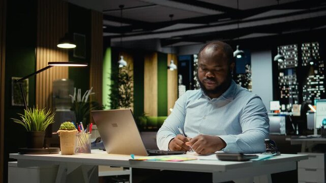Black office employee ripping a piece of paper after making a mistake, restarting his task in anger and tearing up the page sheet. Discontent guy writes a typo while transcribing. Camera A.