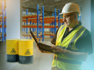 Nuclear safety engineer monitors radioactive waste barrels, using laptop to ensure secure handling, storage and radiation protection in industrial facility.