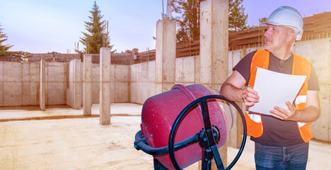 Construction worker inspecting foundation work at a building site, holding project plans near a...