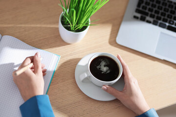 Woman with notebook and pencil having coffee break at wooden table, above view