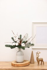 Fototapeta premium Beautiful composition with fir tree branches in vase and reindeer figure on wooden table near white wall indoors. Winter decor