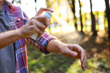 Man spraying tick repellent onto arm in park, closeup