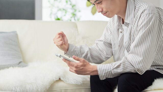 スマホを見てガッツポーズをするアジア人男性