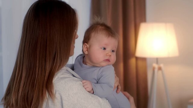 A caring mother cradles her baby in a warm, cozy home environment. The soft lighting enhances the affectionate moment as they share a special bond together.