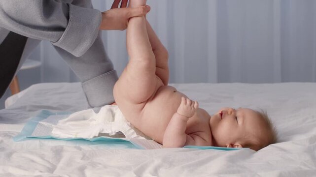 A young child is having a diaper change at home. The caregiver gently lifts the baby's legs, showing a loving interaction. The cozy setting highlights the bond between them.