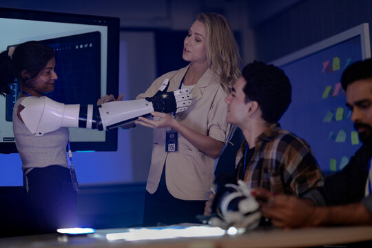 robotics engineers in an RD lab test an AI powered prosthetic. An Indian man tests electronics while a woman presents the bionic arm and another woman wears one.