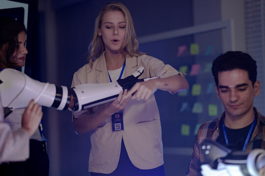 robotics engineers in an RD lab test an AI powered prosthetic. An Indian man tests electronics while a woman presents the bionic arm and another woman wears one. - Powered by Adobe