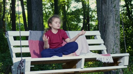 Child meditating outdoors in nature. Peaceful mindfulness moment in forest. Calm breathing and relaxation scene. Healthy lifestyle and mental balance. Serenity and harmony in childhood.