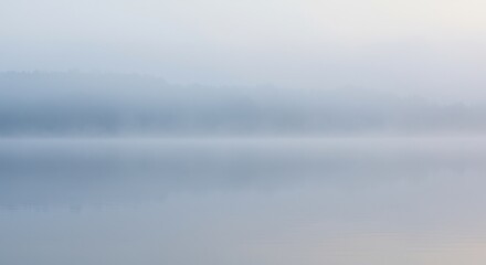 Fototapeta premium Foggy lake Trees are shrouded in mist with water reflections in muted blues and whites