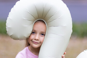 Young girl smiling while holding a large question mark-shaped balloon outdoors