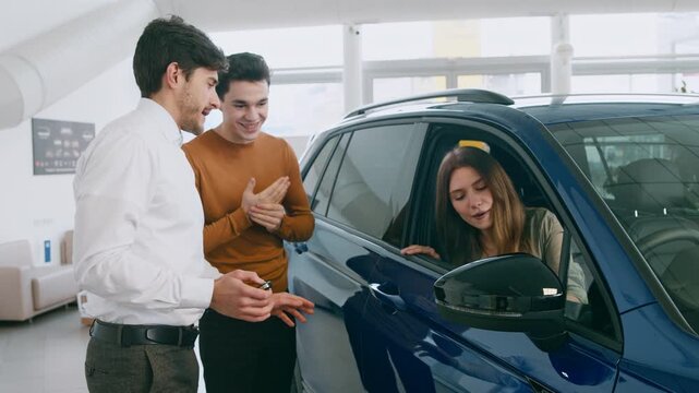 Two young men engage with a car sales associate while a woman inspects a vehicle inside a bright and modern auto salon, showcasing options for leasing and renting cars.