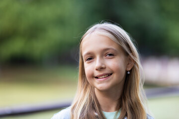 Smiling young girl with long blonde hair standing outdoors in park