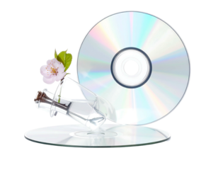 Two CDs lie below a vase with a flower. Silver media with floral accent, against a black background