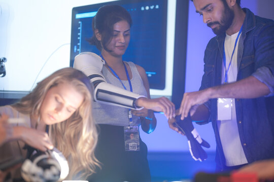 A diverse tech team, including a Caucasian woman, works on robotic arm prototypes. They are in a lab, focused on assembling futuristic prosthetic components at night.