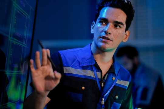 A male engineer smiles, satisfied with the results of an AI system. He is using a stylus on a digital interface in a smart factory command center (SOC) or control room. - Powered by Adobe