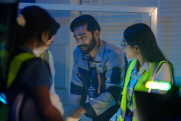 An Indian male engineer in a uniform speaks to his female colleagues. The diverse team, including...