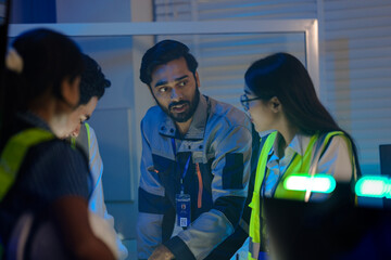 An Indian supervisor leads a night shift briefing in a smart factory control room. He discusses an...