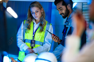 A diverse engineering team, a smiling Caucasian woman in a safety vest and an Indian man,...
