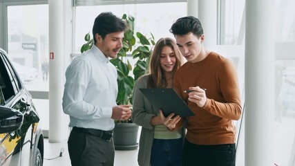 A couple consults with a sales representative in an auto salon, reviewing leasing options. They appear engaged and focused on choosing the right car for their needs in a modern setting.