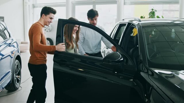 A group of millennials engages with a car sales representative while looking at a sleek black vehicle. They appear excited about the possibilities of buying or leasing a new auto.