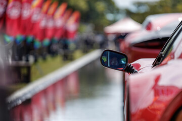 Stylish flexible black rubber jointed mirror mounted on red sports car parked in reflecting pool at auto exhibition symbolizes attention to flowing design of cars sleek elegant contours.