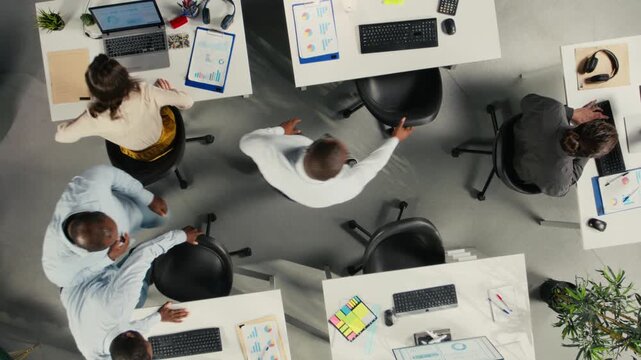 Top down view zoom in of business people using computers in workspace, analyzes projections and reports. Team focuses on business intel, insights and targets under executive management. Camera A.
