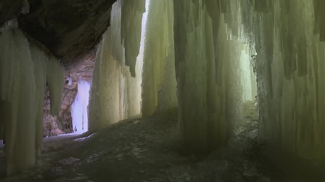 Tall vertical ice sheets rise from the ground inside Eben Ice Caves, tilt up view showing hanging icicles and cave roof