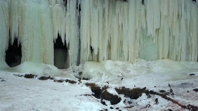 Upward view of Eben Ice Caves entrances with massive thick icicles beneath forest in winter, USA.