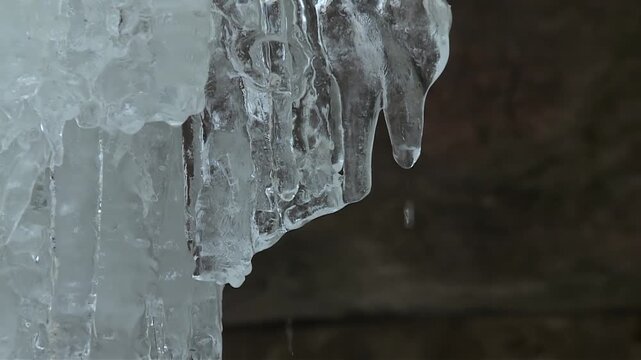 Crystal clear icicle hangs from a frozen cluster inside the Eben Ice Caves in Michigan, with water droplets forming at the tip.