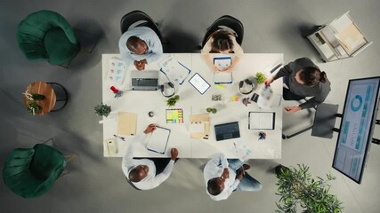 Top down view of diverse colleagues and managers participating in briefing. Business meeting focuses on negotiation, reporting and resource allocation for corporate development and success. Camera A. - Powered by Adobe