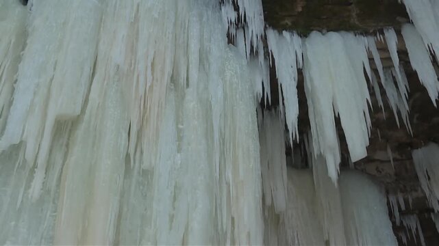 Close up view of massive, thick icicles cascading in vertical sheets from a rocky ledge at the Eben Ice Caves in Michigan.