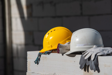 A close-up of two construction helmets, one yellow and one white, resting on a concrete block. The...