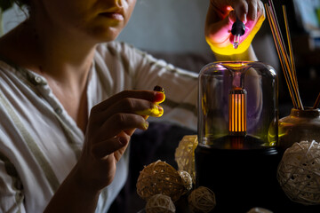 Female hands adding essential oil to Home fragrance aromatic diffuser with essential oil. Modern air humidifier at home. Improving the comfort of wellbeing living in house. Ultrasonic aroma perfume