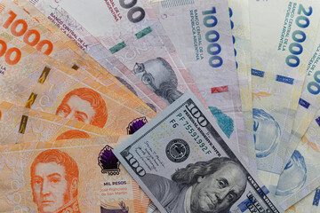  Argentine peso banknotes arranged in a fan covering the entire frame with a 100 US dollar bill placed on top, editorial concept illustrating inflation and exchange rate. Top, aerial view