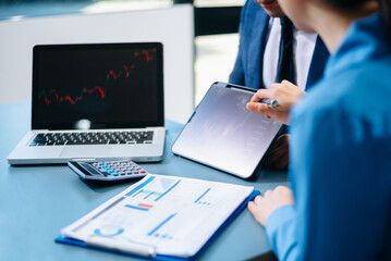 Asian business team analyzing stock charts on tablet and laptop during meeting. Concept of finance, investment strategy, teamwork, and corporate success.