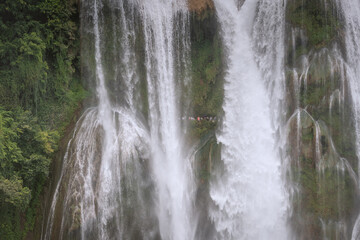 Close up on the water falling and the people walking under the Huangguoshu Waterfall in Guizhou Province, China