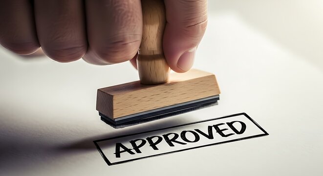 Close up of a hand holding a wooden stamp pressing the word approved onto white paper