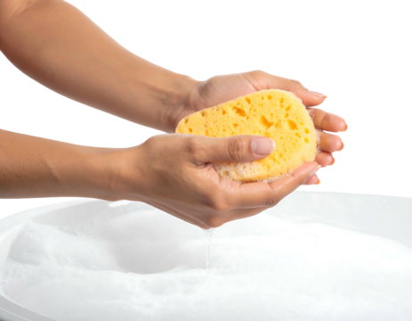 Woman's hands squeezing soapy yellow sponge over white tub filled with bubbly water against a dark backdrop