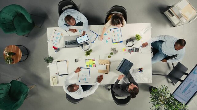 Time lapse top down view zoom in of business people using computers in workspace, analyzes projections and reports. Team focuses on business intel, targets under executive management. Camera A.