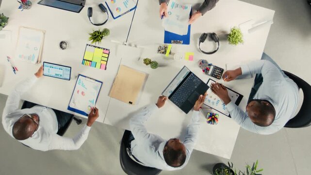 Top down view zoom out of diverse coworkers in meeting discuss budgeting, forecasting plans for efficiency. Corporate team evaluates performance metrics, reports for resources allocation. Camera A.