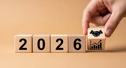 Hand placing a wooden cube with handshake and growth chart icons onto the year 2026 signifying future business success