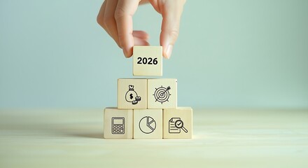 Hand placing a wooden block with the number 2026 on top of a tower of blocks representing future goals and aspirations
