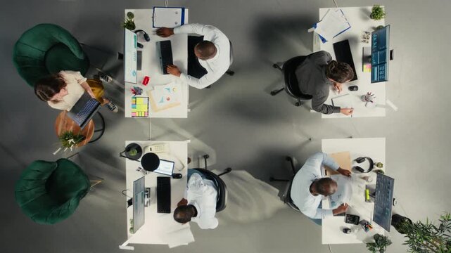 Time lapse top down view zoom in of diverse work team study analytics and forecasting, focus on performance metrics and report writing. Data visualization to support management decisions. Camera A.