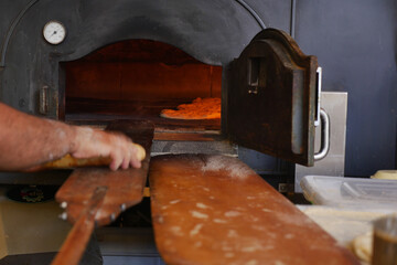Pizza chef sliding dough into traditional oven