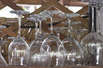 Upside down collection of empty, clean wine glass stemware at bar. transparent glassware hangs from wooden rack in restaurant, waiting for beverage or celebration