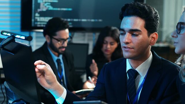 A diverse tech team is collaboratively analyzing code on a computer screen in office. Supervisor points to key data and explaining project to a software developer. App or program development