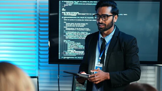 Professional man presenting software code on a screen in a modern office. Developer discusses programming, data security, or tech business strategy. Cybersecurity meeting with team