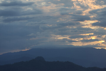 Dramatic mountain silhouette against beautiful cloudy sky at sunset. serene landscape shows peaceful evening light breaking through dark, moody cloud cover